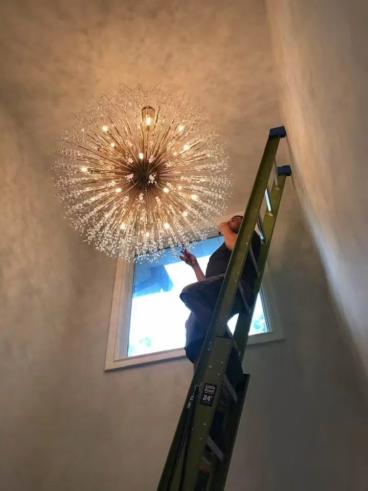 Worker on a ladder installing a decorative chandelier